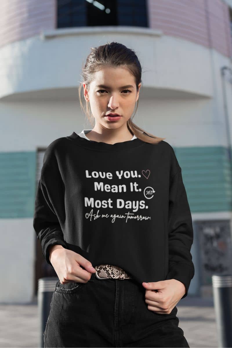 funny couples pullover with a woman wearing a black sweatshirt with a printed message, standing in front of a building.