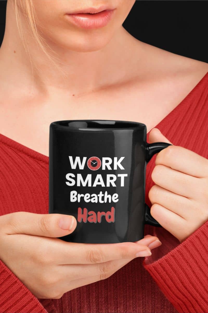 funny coworker coffee mug with a person holding a black mug with 'Work Smart Breathe Hard' text in red and white.
