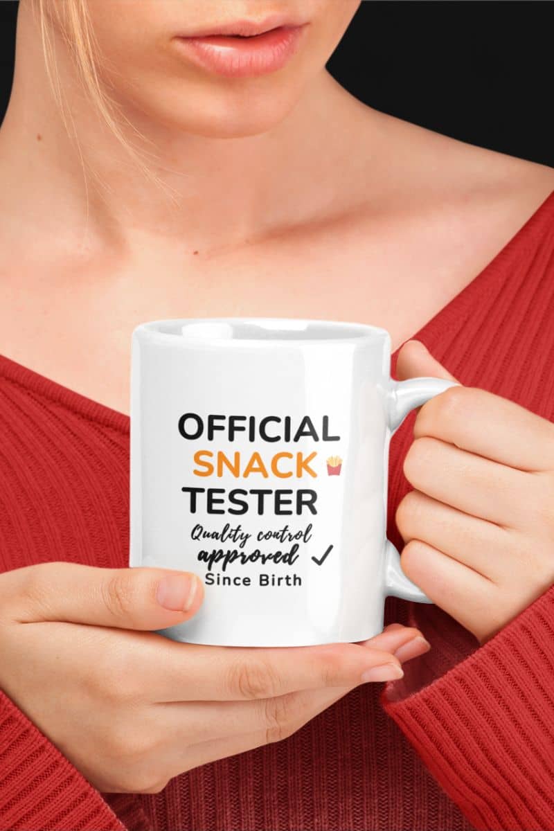 funny coworker mugs with a person holding a white mug with text 'Official Snack Tester – Quality Control Approved – Since Birth' in a red top.