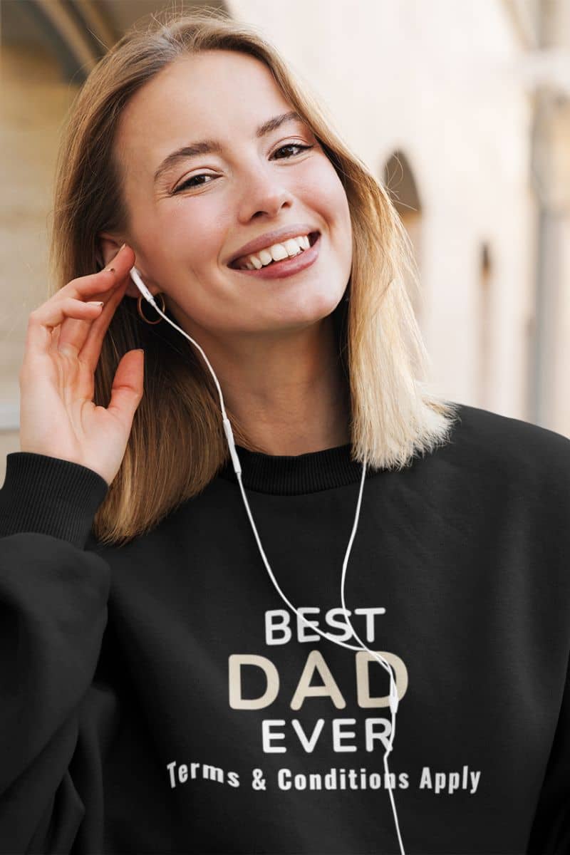 funny dad sweater with a woman wearing a black sweatshirt with 'Best Dad Ever, Terms & Conditions Apply' text, listening to music with earphones.