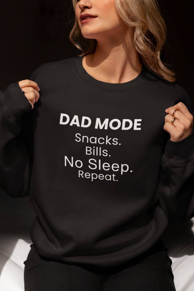 funny dad sweatshirt with a person wearing a black sweatshirt with 'DAD MODE: Snacks. Bills. No Sleep. Repeat.' text.