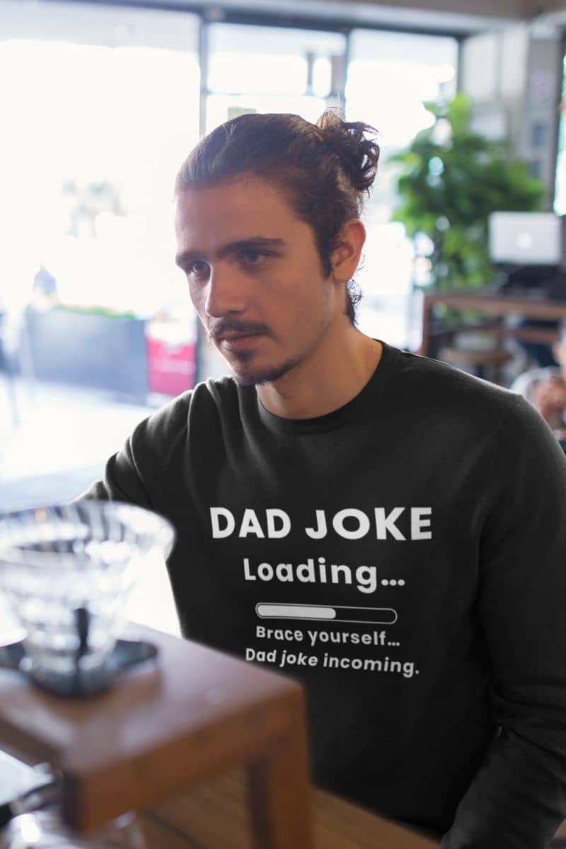 funny dad sweatshirt with a man wearing a black sweatshirt with text 'Dad Joke Loading, Brace yourself…Dad joke incoming.' in an indoor setting.