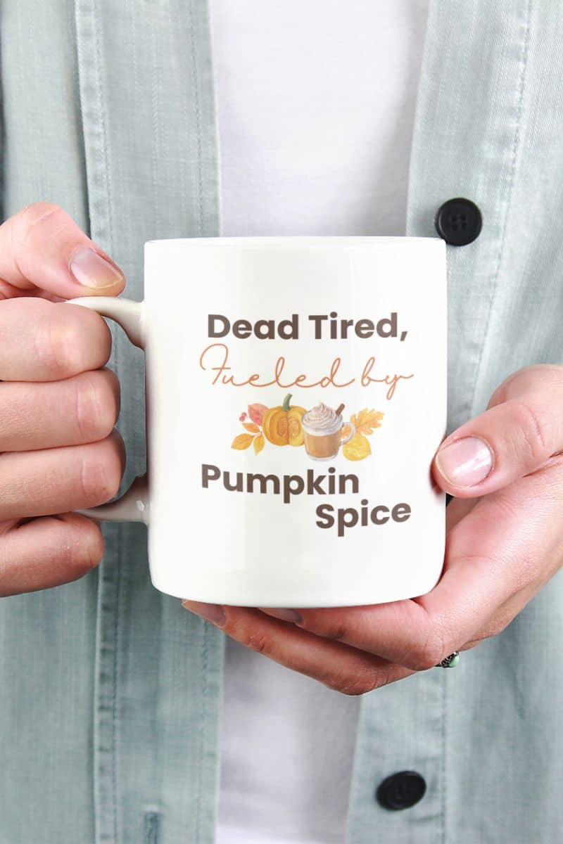funny fall coffee cup with a person holding a mug with 'Dead Tired, Fueled by Pumpkin Spice' text and graphics.