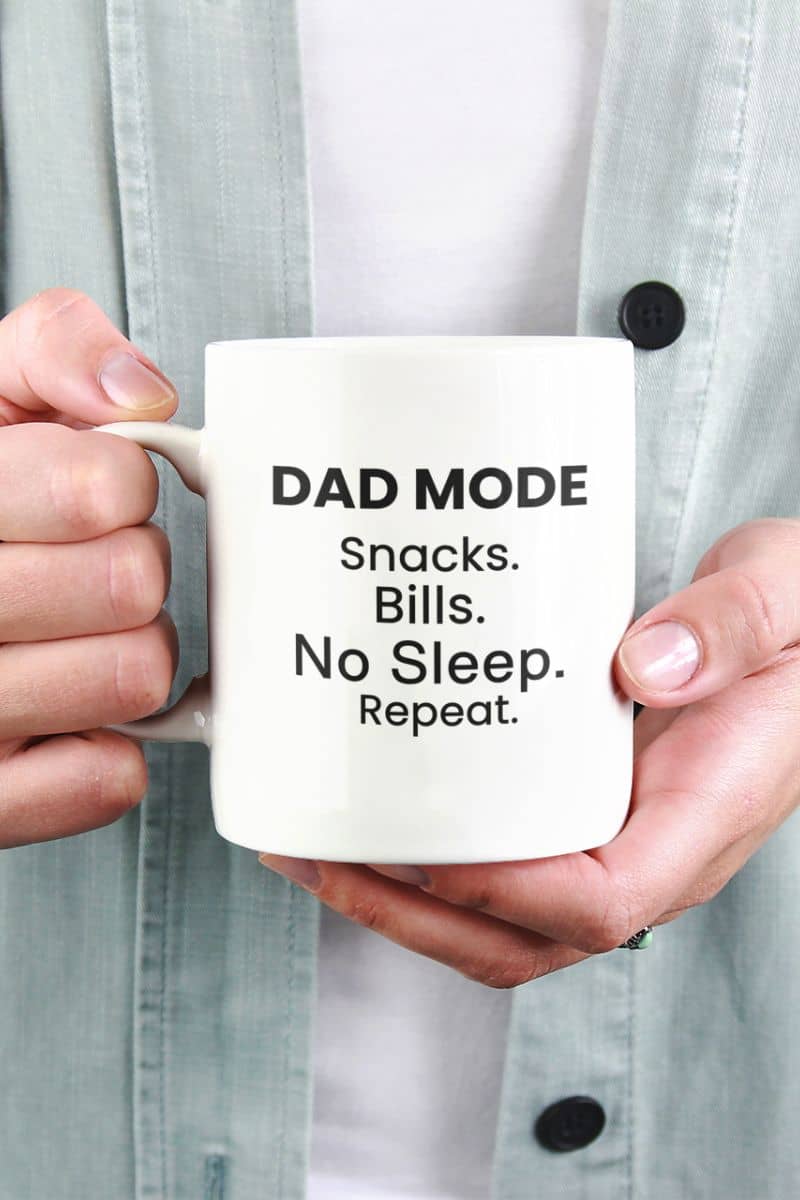 funny father mug with a person holding a mug with text 'DAD MODE: Snacks. Bills. No Sleep. Repeat.'.