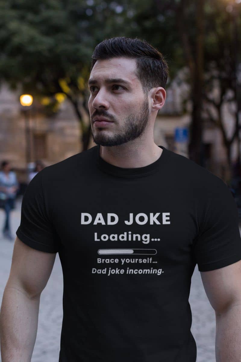 funny father shirt  with a man wearing a black t-shirt with text 'Dad Joke Loading, Brace yourself…Dad joke incoming.' in an urban setting