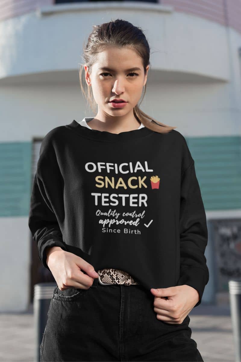funny graphic sweatshirt with a person wearing a black sweatshirt with text 'Official Snack Tester – Quality Control Approved – Since Birth', standing in front of a building.