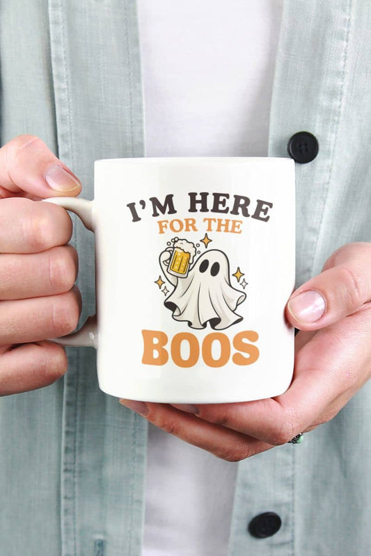A person holding a funny Halloween mug featuring an “I’m Here for the Boos” graphic of a ghost holding a beer mug