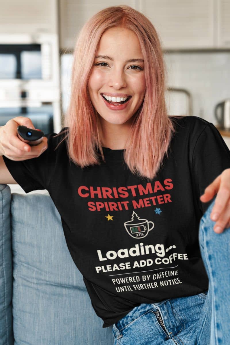 funny holiday coffee shirt with a person wearing a black t-shirt with a humorous Christmas design, sitting on a couch.