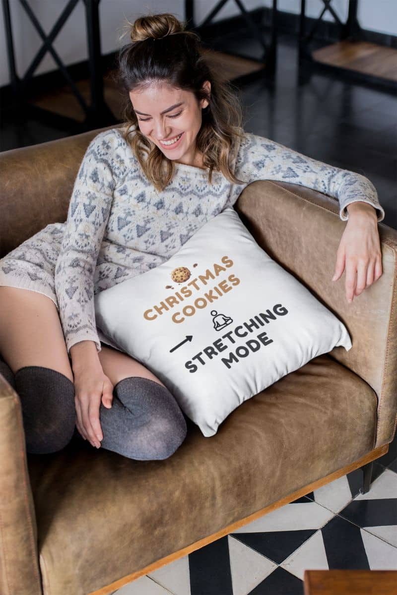 funny holiday pillow with a woman sitting on a couch with a pillow that reads 'Christmas Cookies, Stretching Mode' and 'Stretching Mode'.