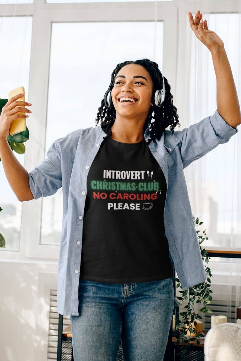 funny holiday tee with a girl in a black t-shirt with text 'Introvert Christmas Club, No Caroling Please', dancing to music