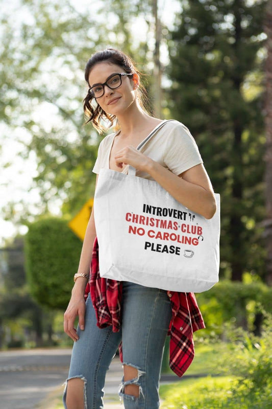 funny holiday tote with a woman holding a tote bag with text 'Introvert Christmas Club, No Caroling Please' outdoors
