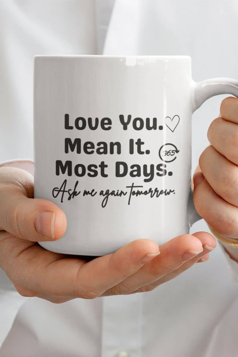 funny love mug with a person holding a white mug with text 'Love You. Mean It. Most Days. Ask me again tomorrow.'