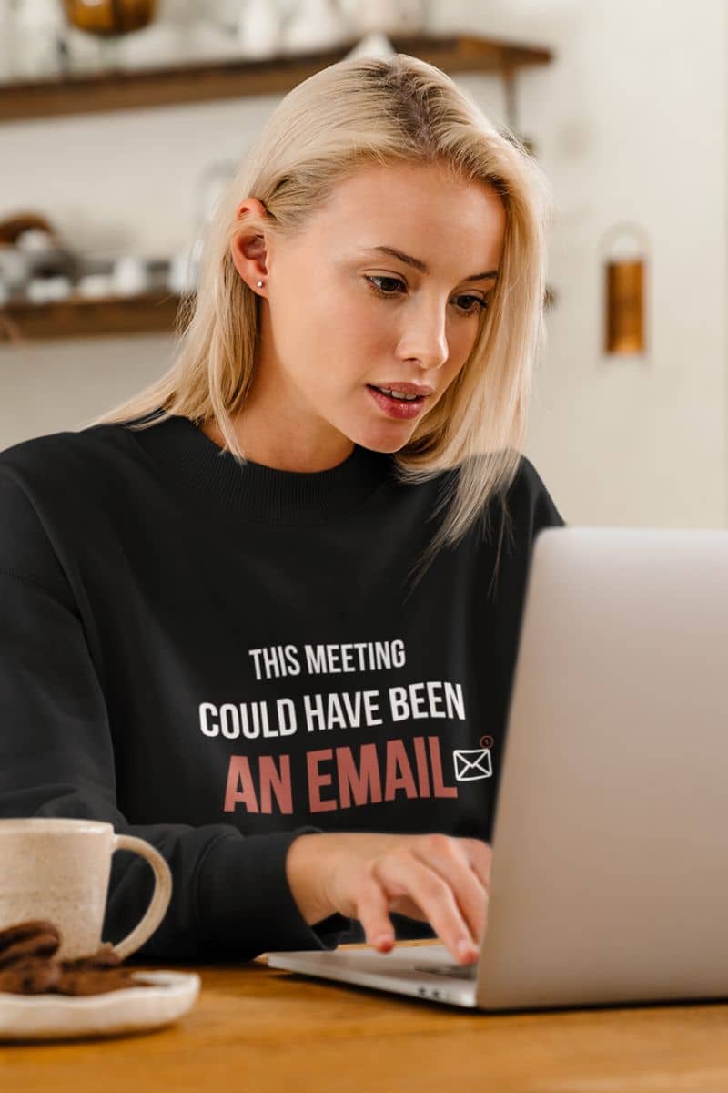 funny meeting sweatshirt with a woman wearing a black sweatshirt with humorous text 'This Meeting Could Have Been An Email', using a laptop in a kitchen.