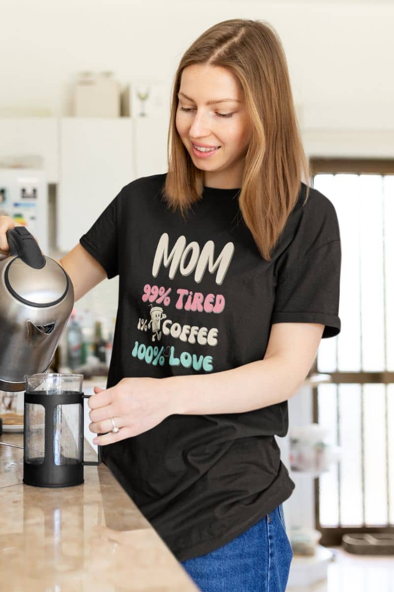 funny mom shirt with a woman in a kitchen wearing a black t-shirt featuring the text 'Mom 99% Tired, 1% Coffee, 100% Love''.
