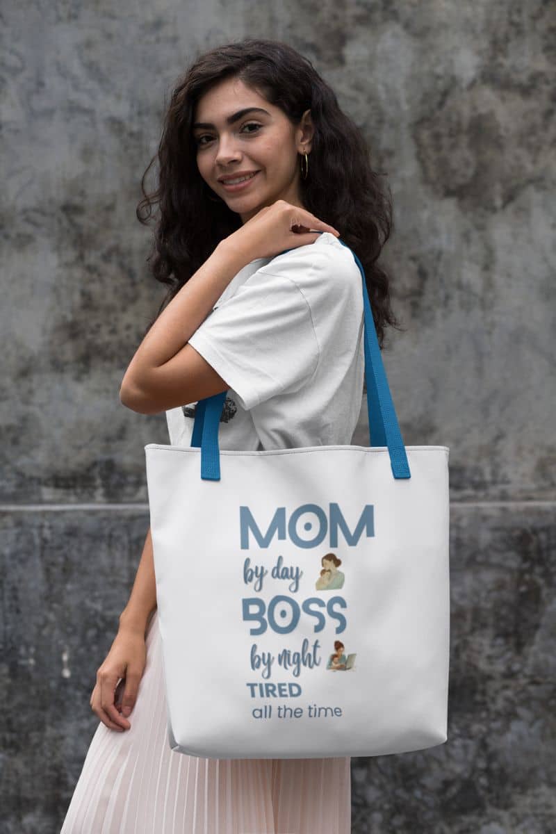 funny mom tote bag with a woman holding a tote bag with text and graphics against a textured wall.