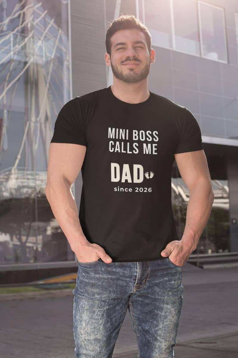 funny new dad shirt with a man wearing a black t-shirt with text 'Mini Boss Calls Me Dad – since 2026' standing outdoors.