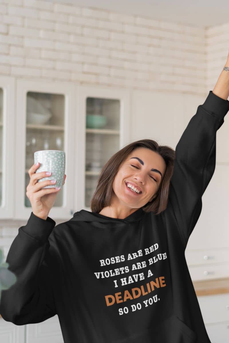 funny office hoodie with a person wearing a black hoodie with humorous text 'Roes are red, violets are blue. I have a deadline so you do', holding a mug in a kitchen.