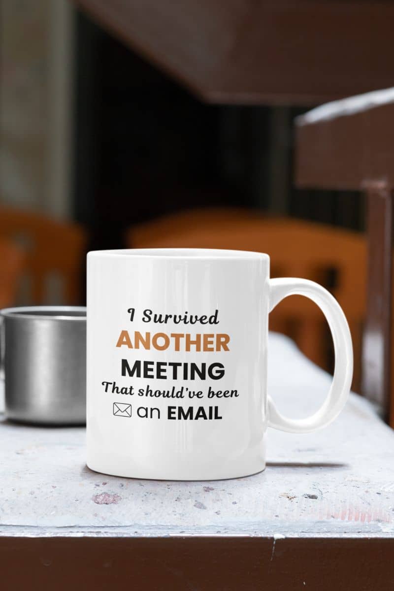 funny office mug with a white mug featuring the text 'I Survived Another Meeting That Should’ve Been an Email' on a table in a cafe setting