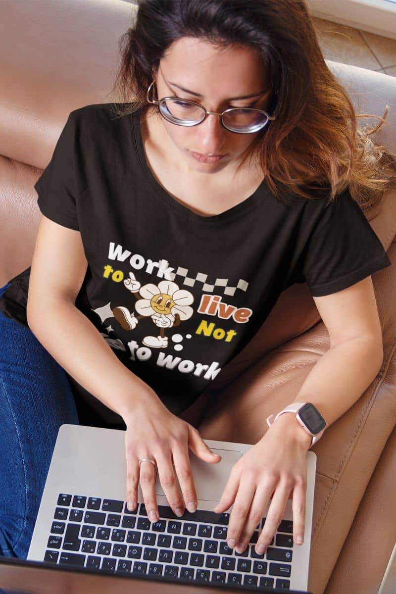 funny office shirt with a woman wearing a black t-shirt with the quote 'Work to Live, Not Live to Work' while using a laptop.
