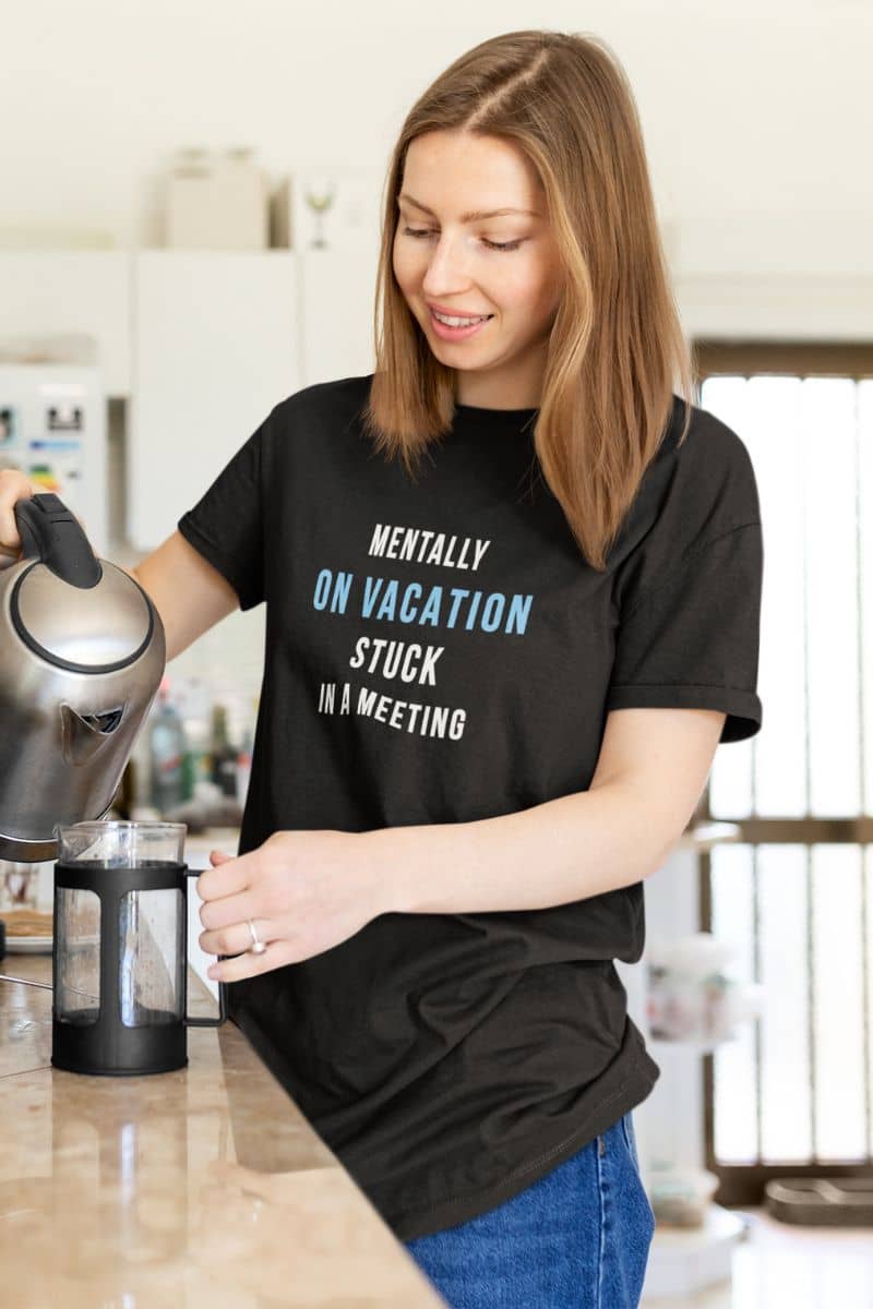 funny office tee with a woman wearing a black t-shirt with text 'Mentally on Vacation. Stuck in A Meeting', pouring from a kettle.