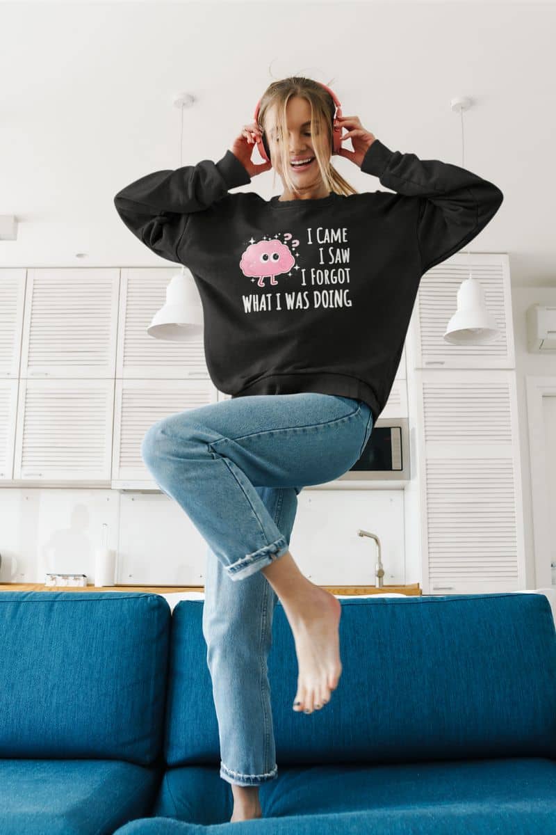 funny quote sweatshirt with a person wearing a black sweatshirt with a graphic and text 'I came, I saw, I forgot what I was doing', sitting on a blue couch in a room.