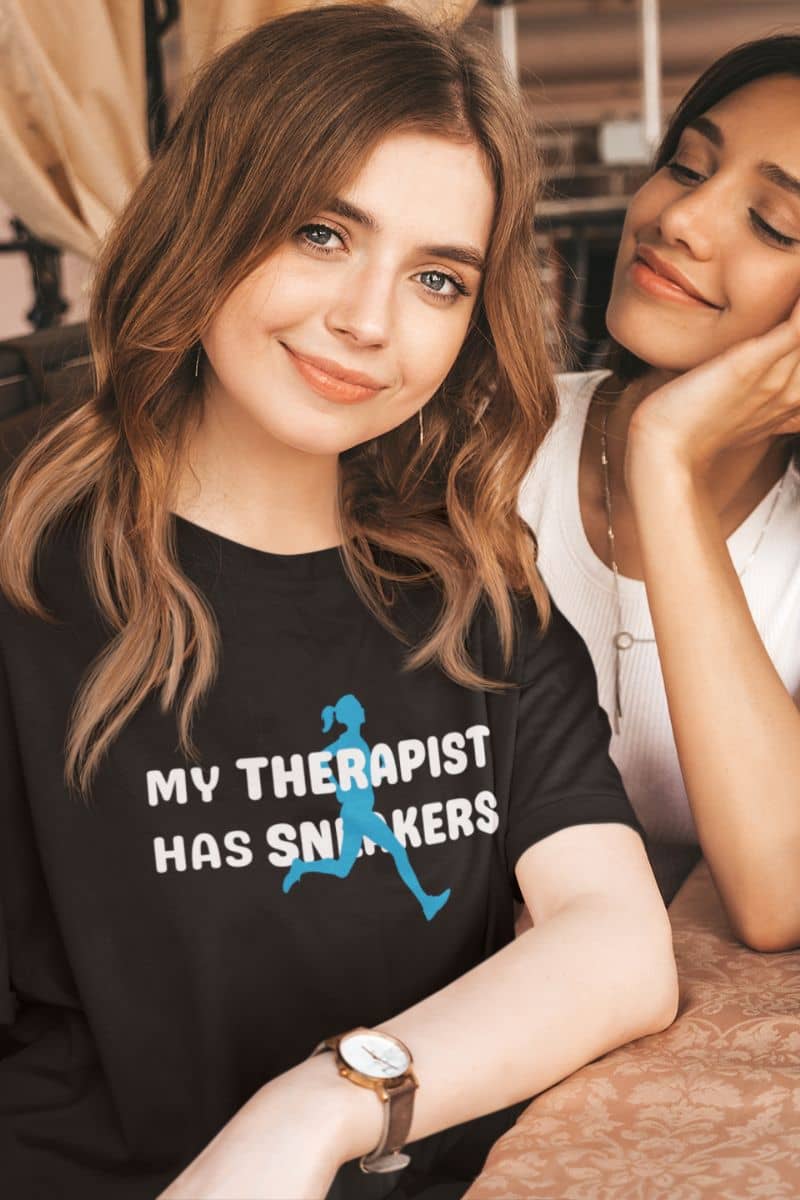 funny runner shirt with a woman wearing a black t-shirt with 'My Therapist Has Sneakers' text and graphic, sitting next to another person.