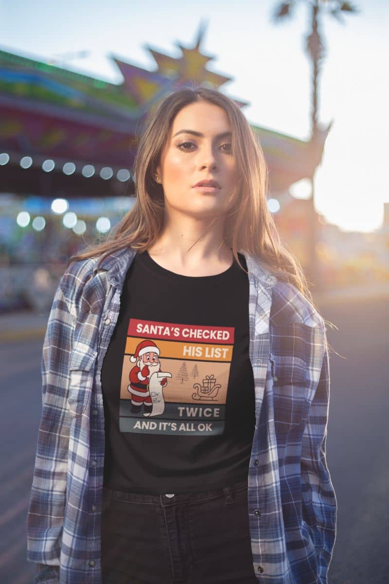 funny santa shirt with a woman wearing a black t-shirt with text 'Santa's Checked His List Twice And It's All Ok' in an outdoor setting