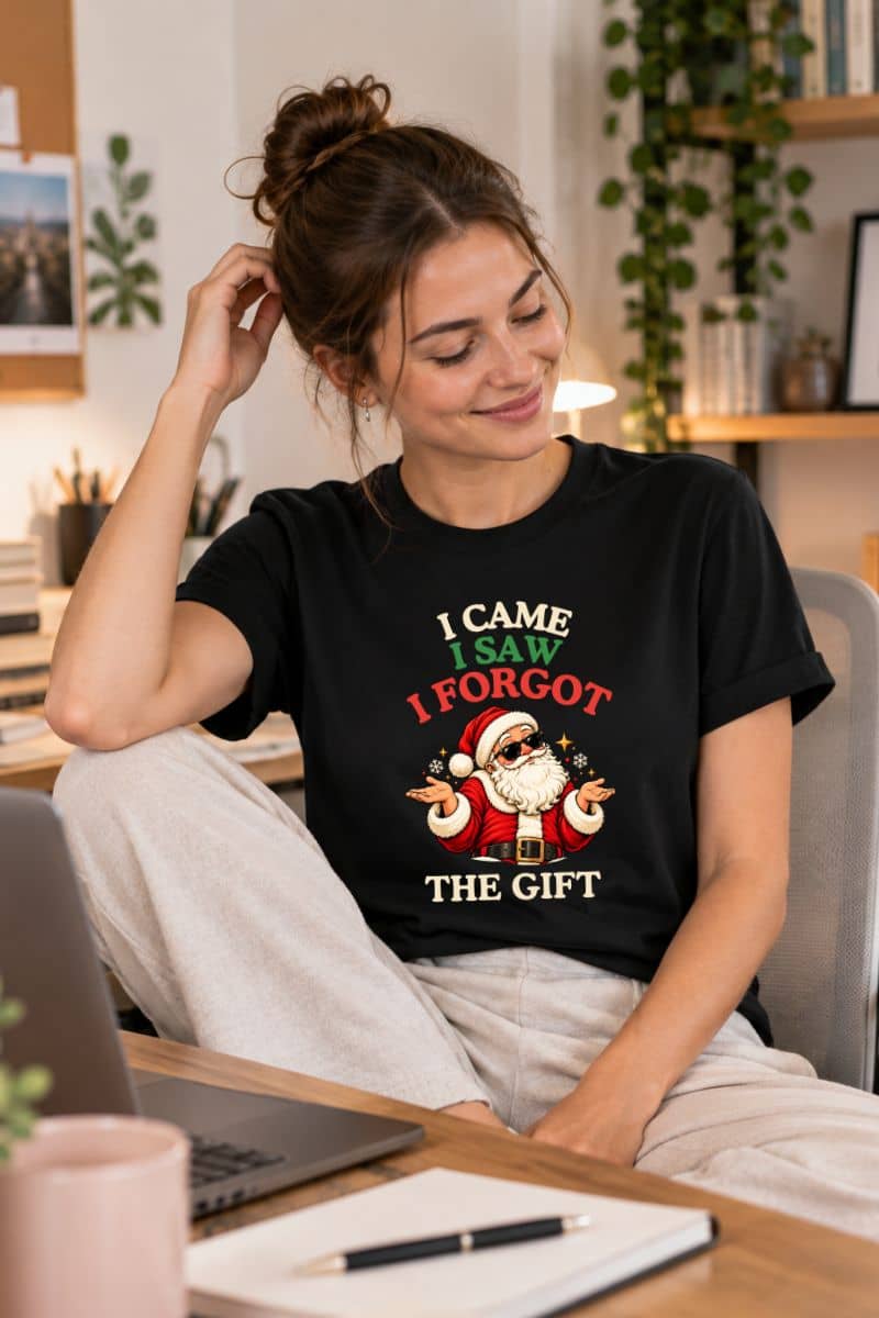 Woman relaxing at her home desk in a black funny Santa shirt with a sunglasses-wearing Santa and “I Came. I Saw. I Forgot the Gift” quote.