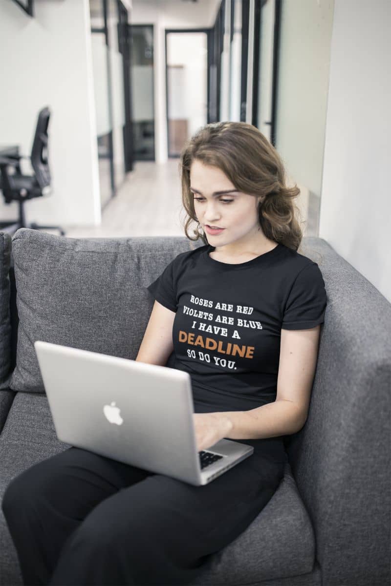 funny t shirts about work with a person sitting on a couch using a laptop with a black t-shirt featuring text 'Roes are red, violets are blue. I have a deadline so you do'.