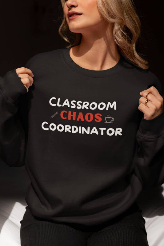 funny teacher sweatshirt with a woman wearing a black crewneck sweatshirt with the text 'Classroom Chaos Coordinator' printed on the front in white and red, holding the sides of the sweatshirt to show the fit.