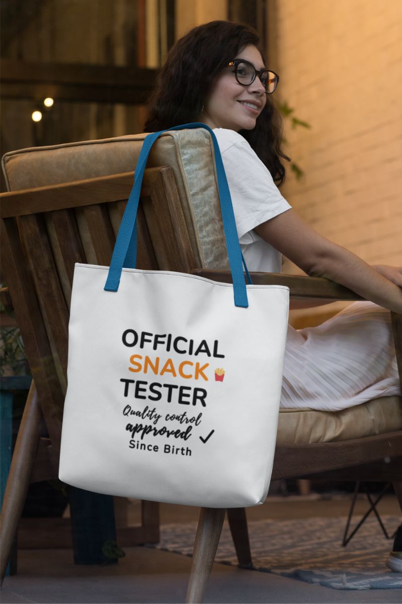 funny tote bag for food lovers with a woman sitting on a chair holding a tote bag with text 'Official Snack Tester – Quality Control Approved – Since Birth'.
