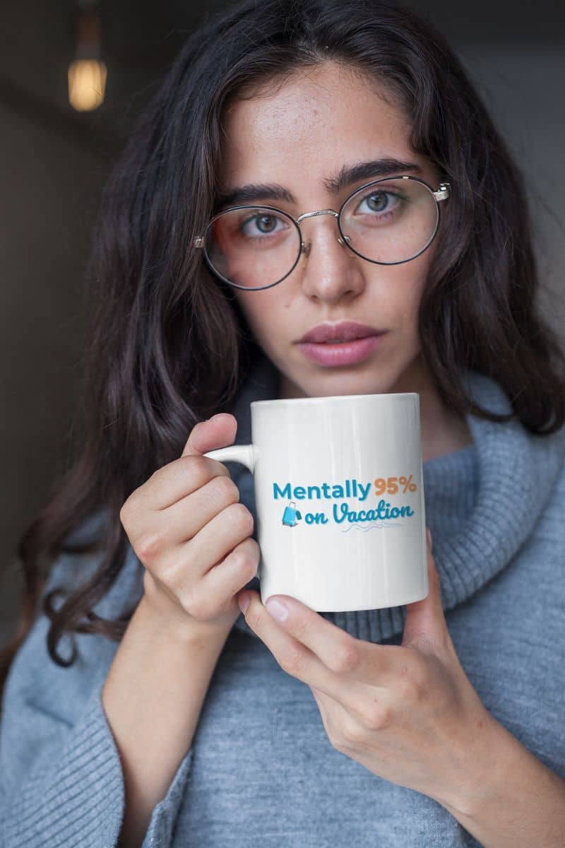 funny travel coffee mug with a woman holding a mug with text 'Mentally 95% on Vacation', wearing glasses and a gray sweater.