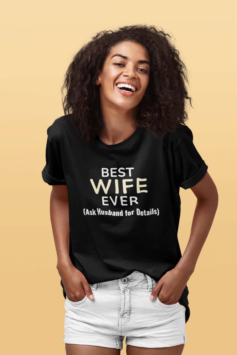 funny wife t-shirt with a woman wearing a black t-shirt with 'BEST WIFE EVER (Ask Husband for Details)' text on a beige background