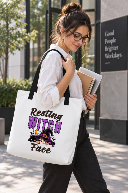 A woman walking outdoors, carrying a white funny witch tote with black handles and a “Resting Witch Face” graphic in purple and black lettering.