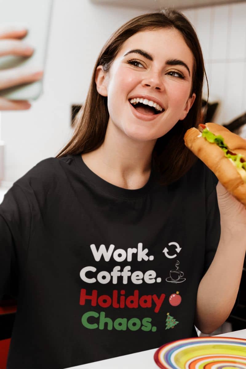 funny work christmas shirt with a person wearing a black t-shirt with text 'Work. Coffee. Holiday Chaos.', holding a hot dog.