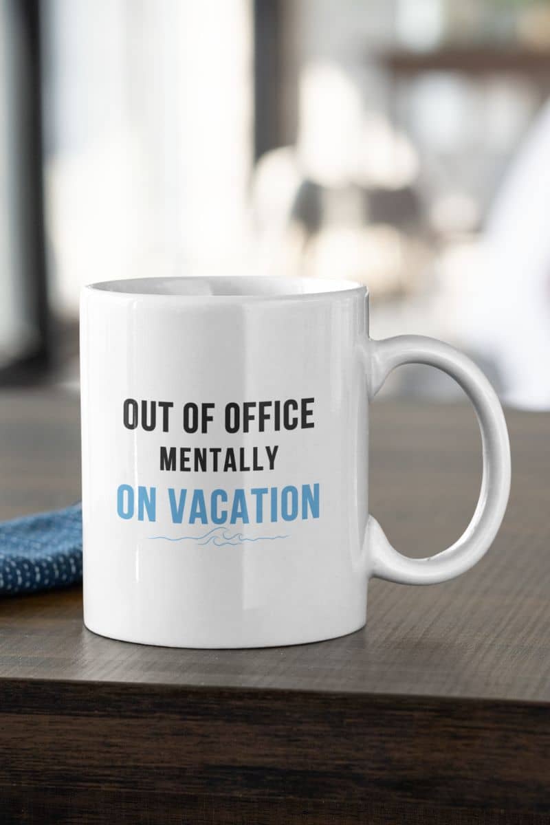funny work mug with a white mug with text 'Out of Office Mentally On Vacation' on a wooden surface.
