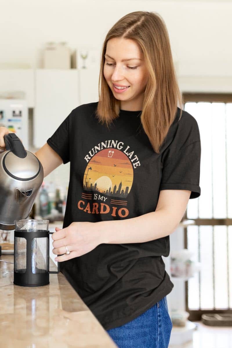 funny work shirt with a woman in a kitchen wearing a black t-shirt with a humorous graphic and text 'Running Late Is My Cardio'