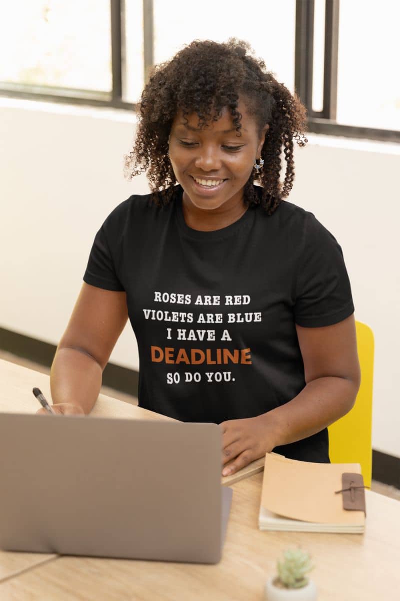 funny work shirts with a person wearing a black t-shirt with a humorous message, sitting at a desk with a laptop.