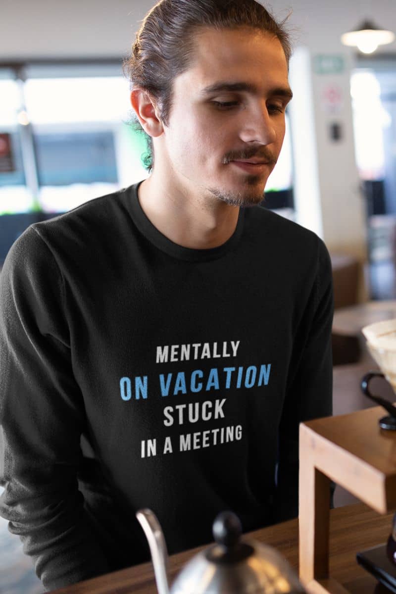 funny work sweatshirt with a man wearing a black sweatshirt with text 'Mentally on Vacation. Stuck in A Meeting' in a casual setting