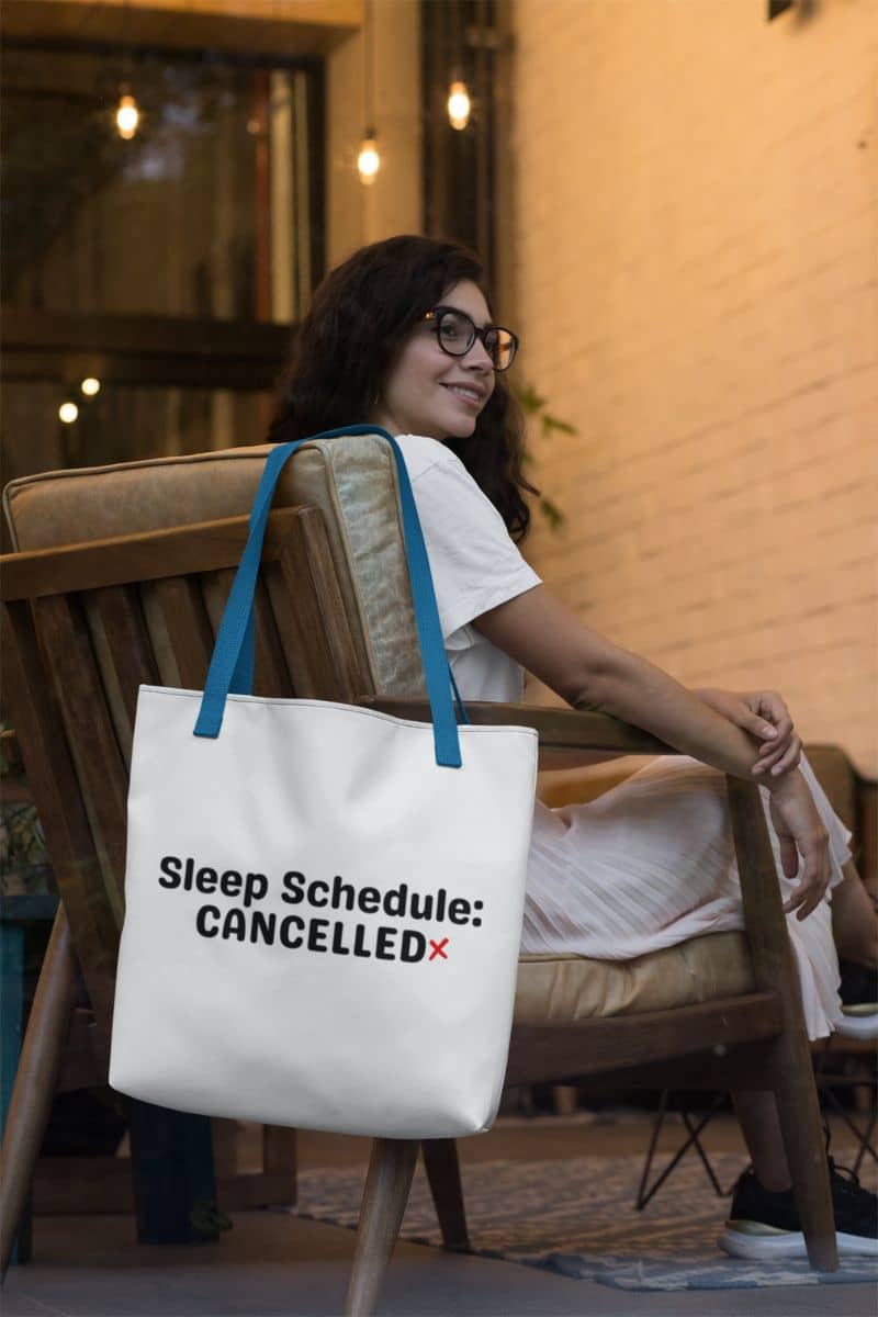 funny work tote with a woman sitting on a chair with a tote bag that says 'Sleep Schedule: CANCELLED'.