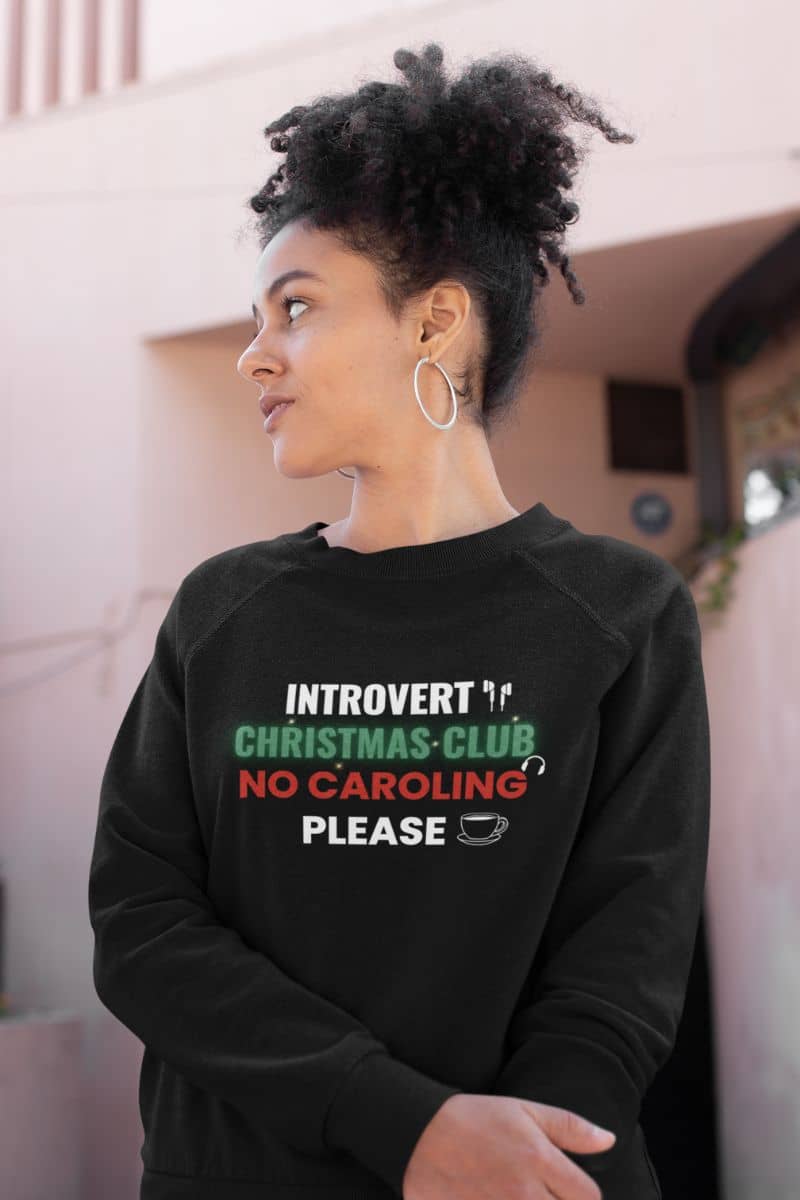 funny xmas sweatshirt with a person wearing a black sweatshirt with text 'Introvert Christmas Club No Caroling Please' in an outdoor setting.