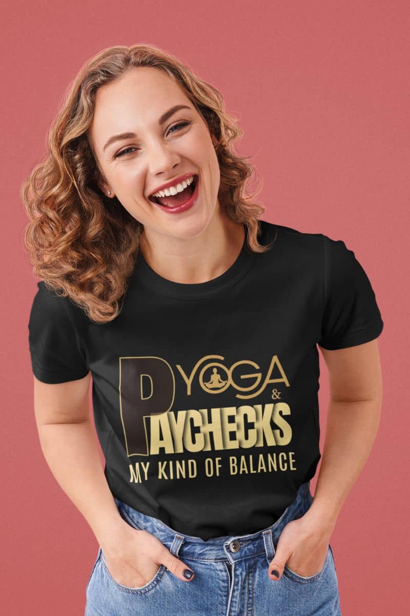 funny yoga shirt for women with a woman wearing a black t-shirt with gold text 'Yoga & Paychecks – My Kind of Balance' against a pink background