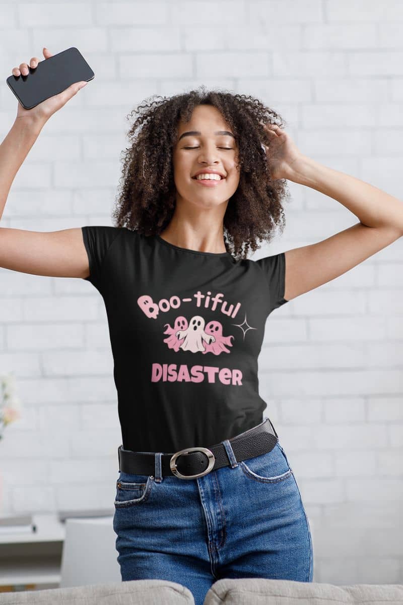 ghost costume t-shirt with a woman wearing a black t-shirt with 'Boo-tiful Disaster' text and design, holding a phone.