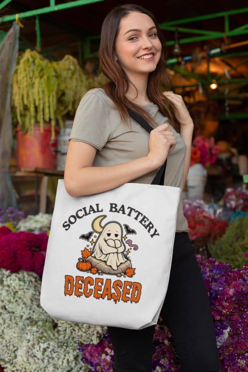 A woman at a flower market carrying a ghost shoulder bag with a ghost and the text 'Social Battery: Deceased' in orange and black.