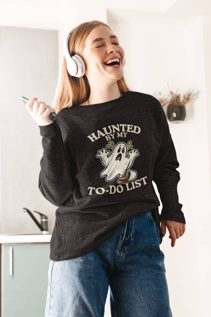 A woman wearing a ghost sweatshirt featuring a “Haunted by My To-Do List” funny ghost, standing in the kitchen