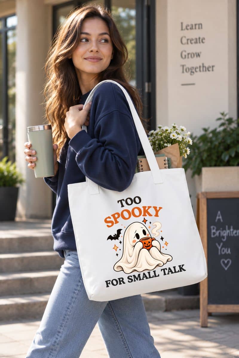 Woman wearing a navy sweatshirt and carrying a white ghost tote bag featuring the “Too Spooky for Small Talk” design.
