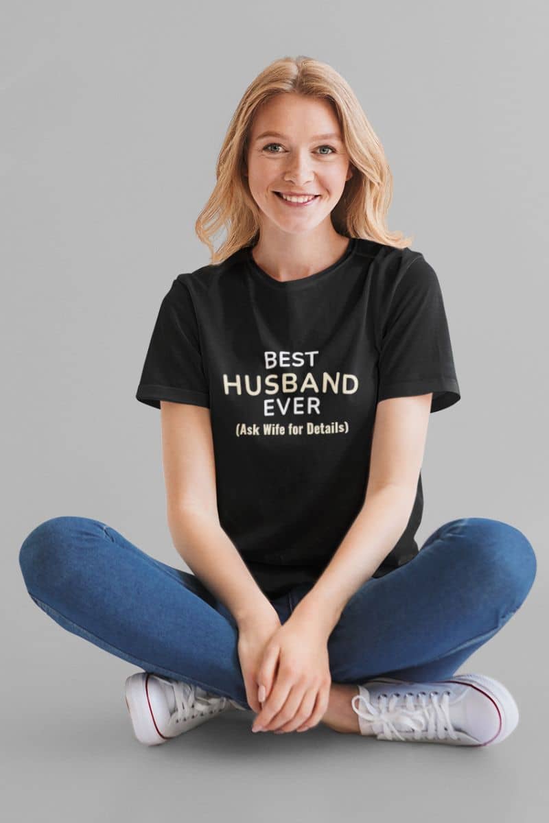 gift for husband shirt with a woman wearing a black t-shirt with text 'Best Husband Ever. (Ask Wife for Details)', sitting on a gray background