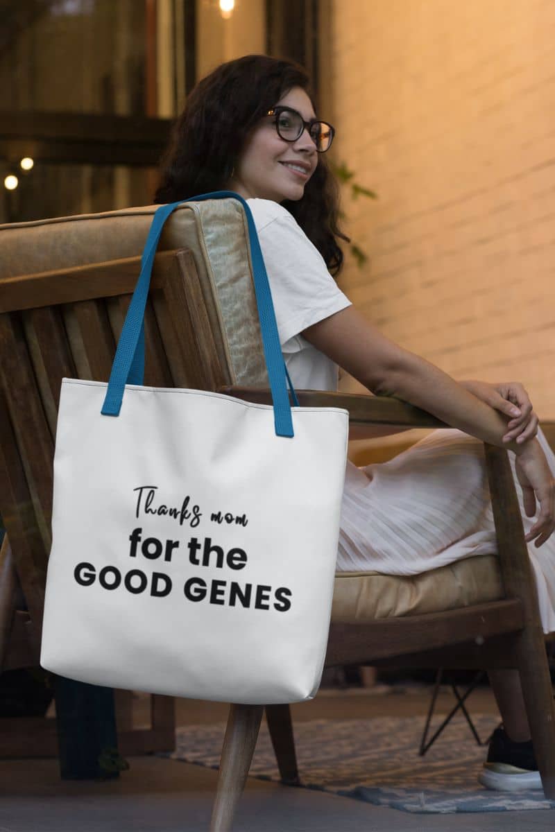 gift for mom tote bag with a woman sitting on a chair holding a tote bag with text 'Thanks Mom for the Good Genes', in an indoor setting.