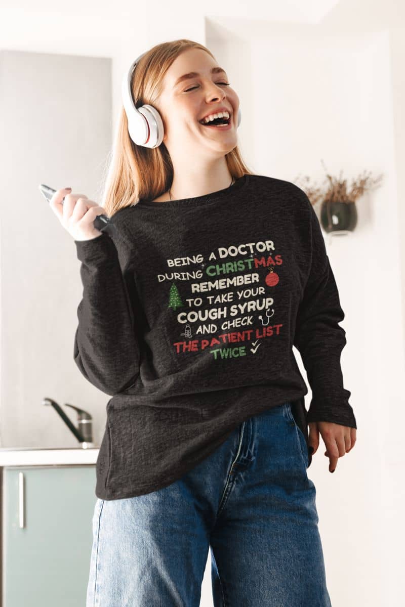 healthcare christmas sweatshirt with a person wearing a black sweater with Christmas-themed text, laughing indoors.