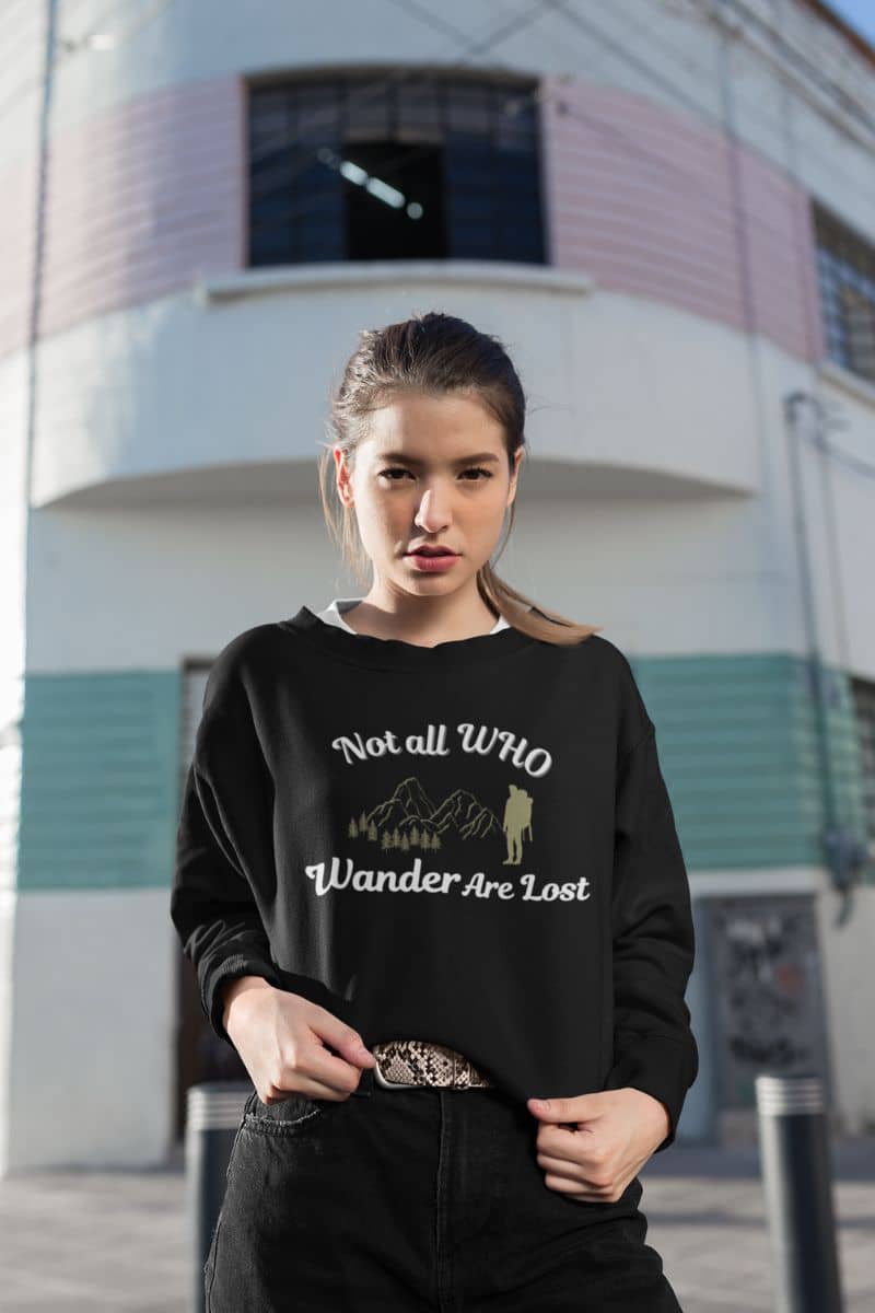 hiking graphic sweatshirt with a woman wearing a black sweatshirt with text 'Not all who wander are lost' and graphics in an urban setting